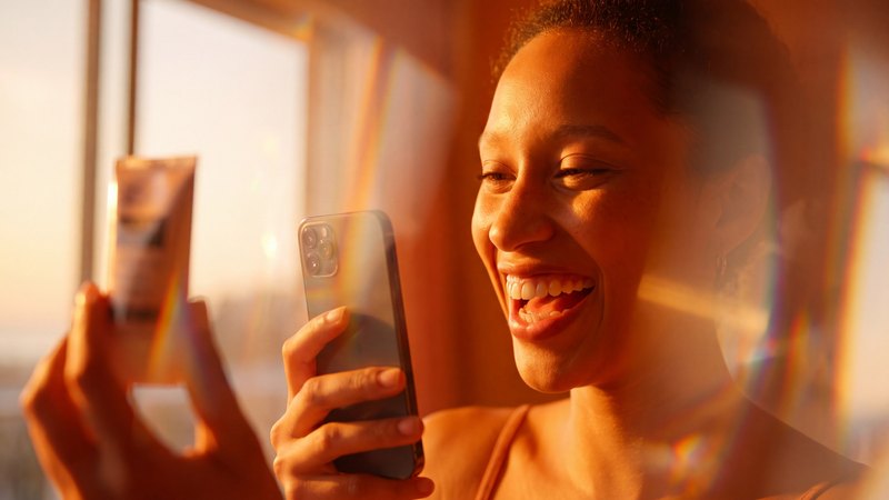 Een creator filmt lachend een product met haar telefoon in tegenlicht
