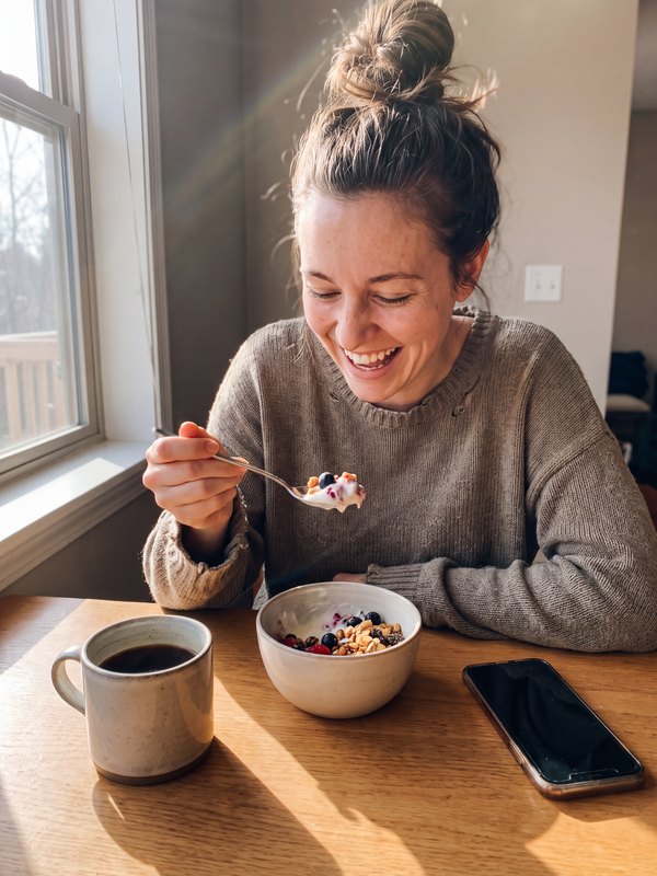 Iemand eet yoghurt met granola aan de keukentafel, een mok koffie ernaast