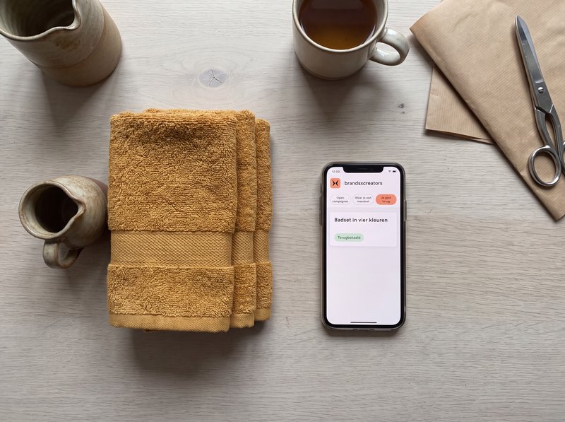 Dezelfde tafel van bovenaf: het uitgepakte product staat rechtop en de telefoon ernaast toont de regel Terugbetaald